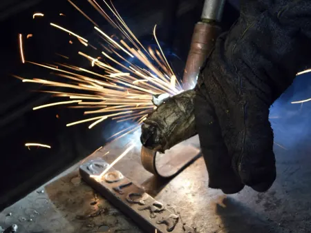 Uma mão de luva a trabalhar metal, entre faíscas.