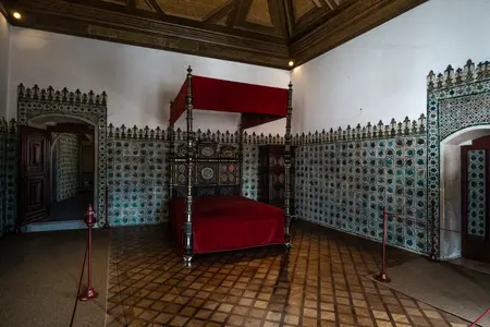 Um quarto com cama de dossel vermelho e paredes de azulejo.