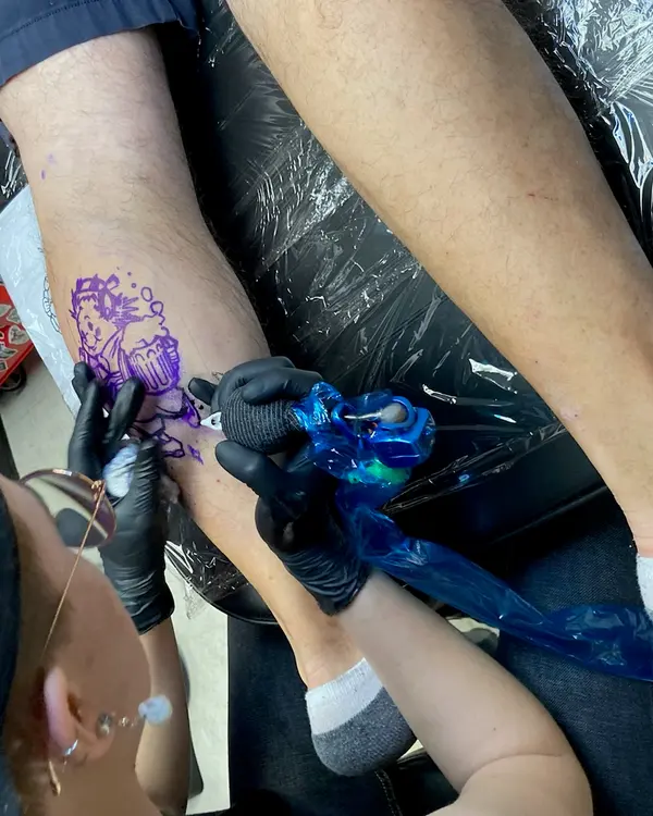 Gloved hands tattooing a design onto a forearm.