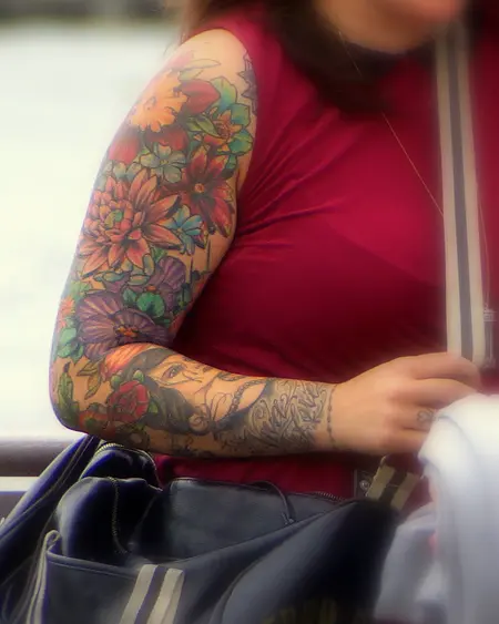 A forearm covered in a colour sleeve of flowers and leaves.